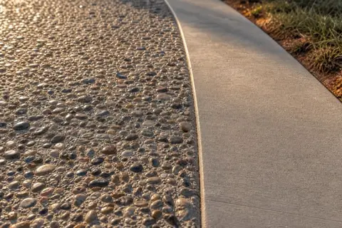 Close view of an exposed aggregate driveway surface with rounded tan and gray pebbles set in concrete after rain